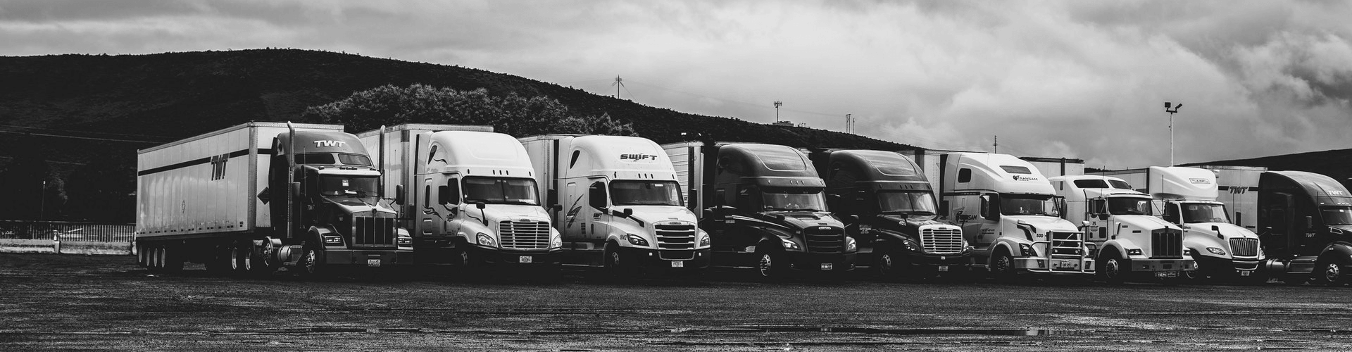 Line of tractor trailers parked in a gravel lot.